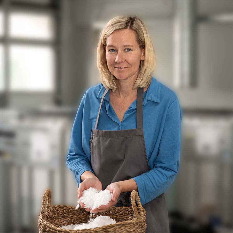 Johanna Jenewein von der Genussmanufaktur Essenz der Alpen steht in ihrer Salzmanufaktur und hält frisch gewonnene, weiße Salzflocken über einem geflochtenen Korb.