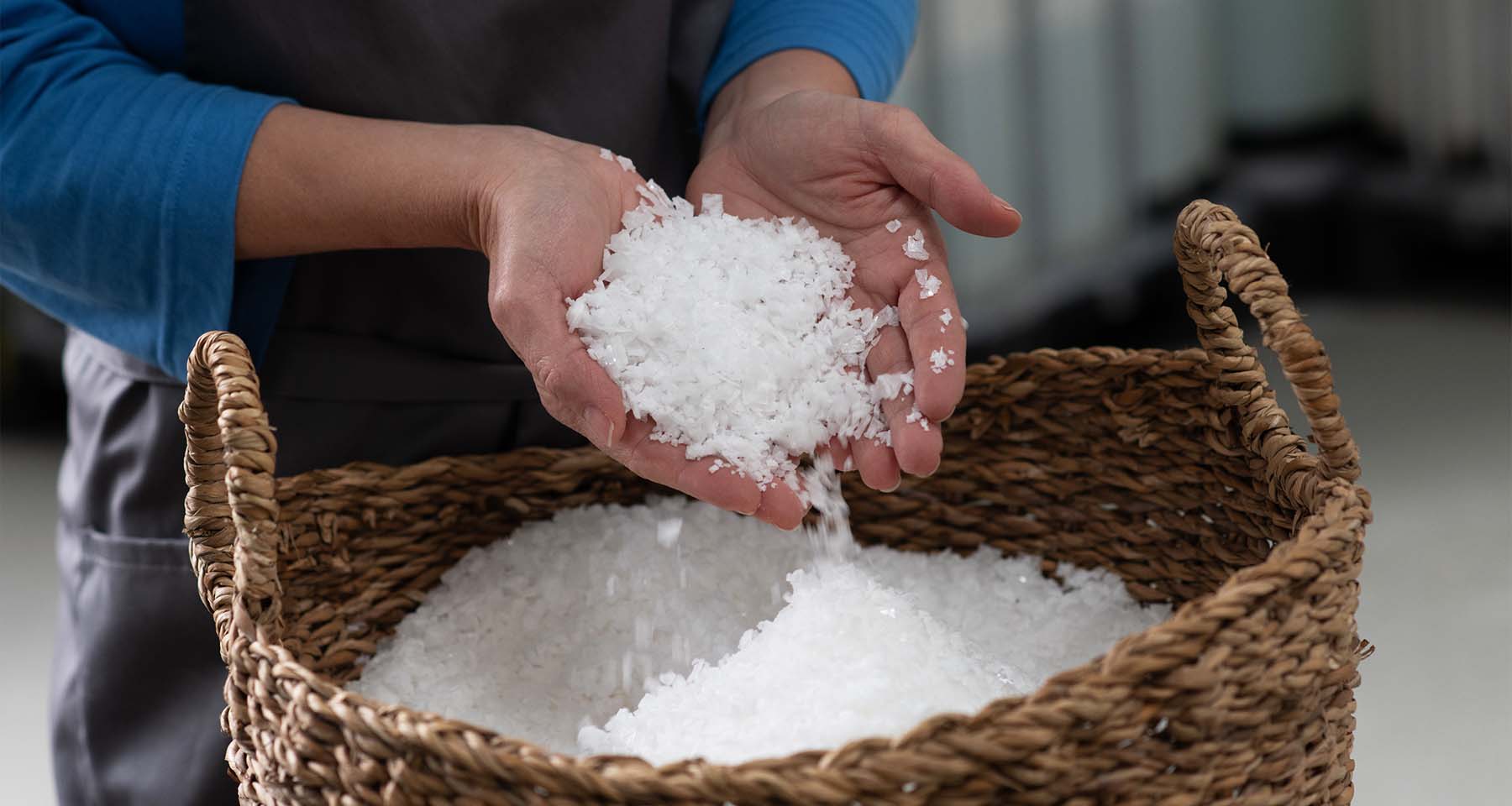 Mitarbeiterin der Genussmanufaktur Essenz der Alpen hält eine Handvoll weißer Salzflocken über einem großen geflochtenen Korb mit frisch gewonnenem Salz.